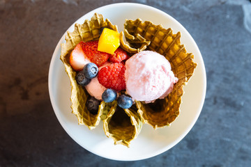 Top view of strawberry ice cream with fresh fruits inside crispy thin waffle bowl.