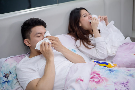 Sick Asian couple sneezing in the bed