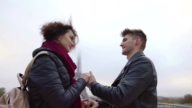 two young lovers are holding hands and flirting against Eiffel tower in Paris in autumn day