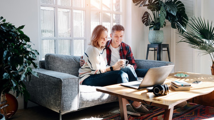 Couple in love at home. Watching TV series using laptop and sitting on the couch together