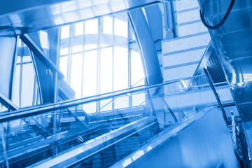 Empty escalator on the background of a large window in a modern station building. Blue toned.