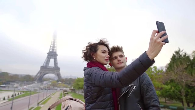 two lovers are taking selfies by smartphone in Paris, photographing their face and Eiffel tower