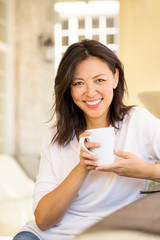 Portrait of an Asian woman smiling and drinking coffee.
