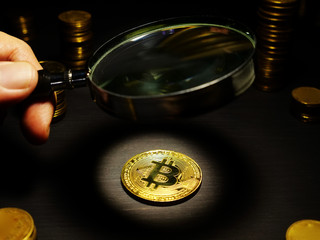 Man looks through magnifying glass on a Bitcoin btc coin. Assessment of crypto cost.