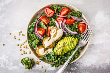 Vegan lentil meatballs salad with kale, avocado, tomato and tahini dressing.