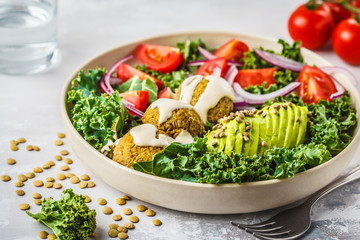 Vegan lentil meatballs salad with kale, avocado, tomato and tahini dressing.