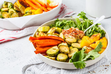 Baked brussels sprouts, zucchini, pumpkin, carrots and hummus salad in a white dish.