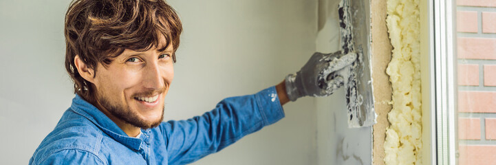 master is applying white putty on a wall and smearing by putty knife in a room of renovating house...