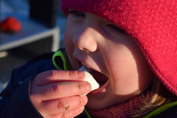 A child in a red hat eats marshmallows. The face of the child close-up. Winter portrait of a girl with marshmallows.