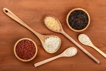 Red long grain Camargue rice, white paella bomba rice, risotto carnaroli, parboiled, jasmine, and wild black rice, shot from the top on a dark rustic wooden background with a place for text