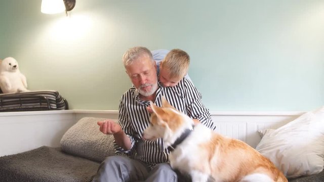 Grandfather and grandson with dog sitting at couch in living room