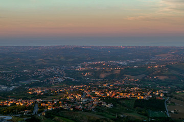 Fototapeta na wymiar Panorama of Republic of San Marino of Borgo Maggiore on the Sunse on the Sunset. From a bird's eye view . Located on Italian peninsula, on the coast of the Adriatic Sea. Italy. European travel.