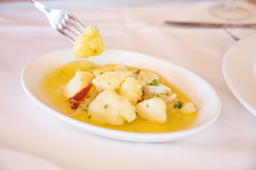 Andalusian potato salad (with onion, olive oil and parsley), in tray with fork taking a piece on white tablecloth
