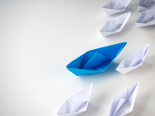 Blue paper boat leading among white ships