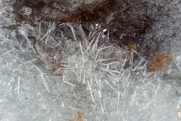 Close-Up Ice Crystals with Snow on the Frozen Winter River with Autumn Yellow Leaves and Dark Brown Stone.