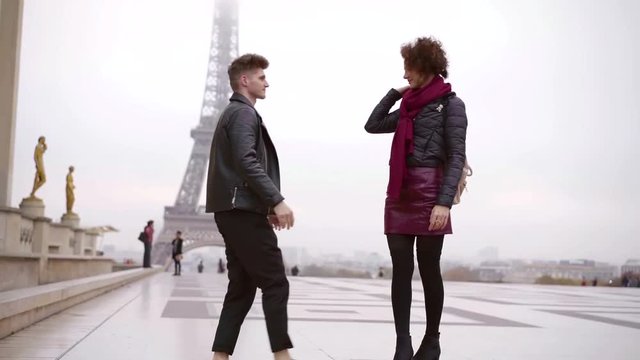 handsome man is approaching to his beloved girlfriend and kissing her, view against Eiffel tower
