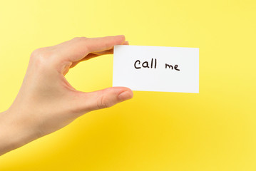 Call me text on a card in woman hand  on a yellow background.