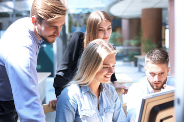 Fototapeta premium Group of young people in casual wear sitting at the office desk and discussing something while looking at PC together.