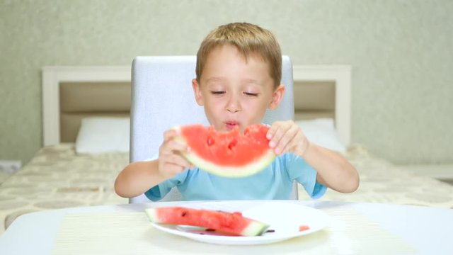 Happy child sitting at the table and with pleasure eats watermelon.