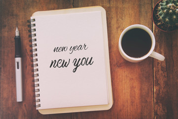Top view of notebook and text NEW YEAR NEW YOU, cup of coffee over wooden desk.