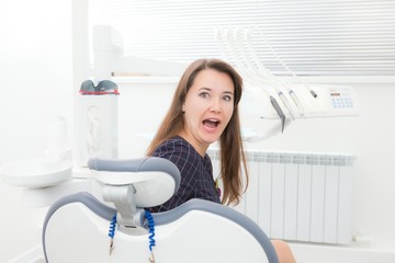 Young female patient sitting on the chair in the dental office. Shocked, surprised, open mouth looking at camera.