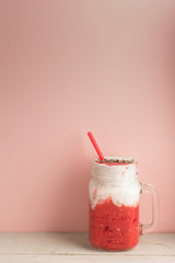 Berry smoothie with yogurt decorated red strow and crushed nuts on white wooden board on pink background with empty space, healthy and delicious breakfast