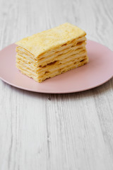 Piece of Napoleon Cake on pink plate over white wooden background, close-up.