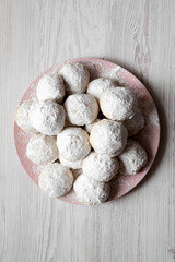 Homemade white mexican wedding cookies on pink plate over white wooden surface, overhead view. Close-up.