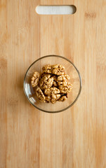 Walnuts in glass bowl on bamboo board, top view. Flat lay, overhead, from above.