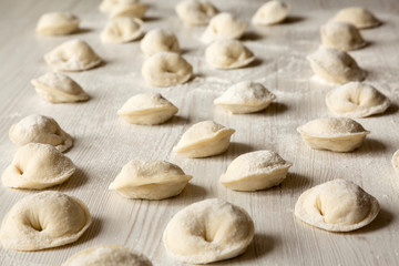 Fototapeta na wymiar Homemade raw tortellini on white wooden surface, side view.