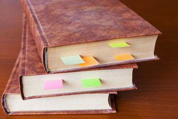 A stack of old books with bookmarks on a wooden table.