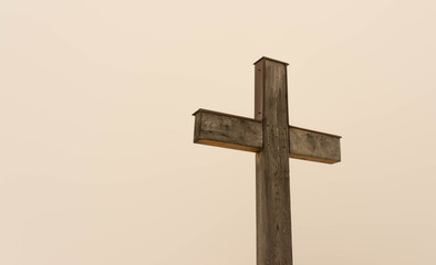 Simple oak wooden cross on natural light, dense fog on the slightly orange background from the sun.