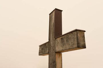 Simple oak wooden cross on natural light, dense fog on the slightly orange background from the sun.