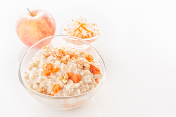Oatmeal with pumpkin and nuts in a glass plate and fresh apple on a white background. Close-up. Copy space