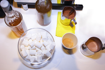 flat lay On a white tabletop in a glass marshmallow cup, two cups of cocoa