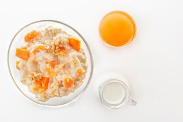 Oatmeal with pumpkin and nuts, a glass of fresh juice, and a jug of milk on a white background. Top view. Copy space.