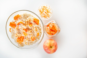Oatmeal with pumpkin and nuts in a glass plate and sliced carrots in a jar on a white background. Copy space. Top view