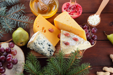 Various type of cheese fruit and honey on wooden boards. Branches of Christmas tree. Swiss cheese, blue cheese, camembert and cottage cheese. Dairy products, lemon, grapes, pears and pomegranate