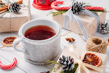 Christmas decorations with gift boxes, pine cones and cup of tea on a white wooden background