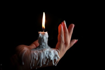White Candle melted on hand in black background. For halloween's or belief concept. Felling darkness with light of flame burning from the supernatural