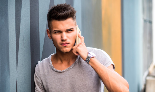 Handsome young man standing outdoors in urban environment next to colorful wall, talking on cell phone