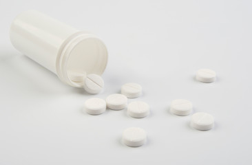 Round white tablets with plastic bottle on white background.