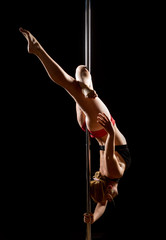 Woman performs pole dance on the stage. Girl whirls around the pole while performing dance or yoga  in the studio. Blonde lady dancing a striptease