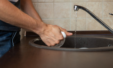 Photo of side of man's hands washing transparent mug in sink