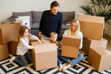 Photo of young parents with children sitting on floor among cardboard boxes