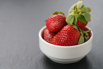 ripe strawberries in white bowl on slate background