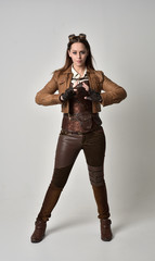 Fototapeta na wymiar full length portrait of brunette girl wearing brown leather steampunk outfit. standing pose, on grey studio background.