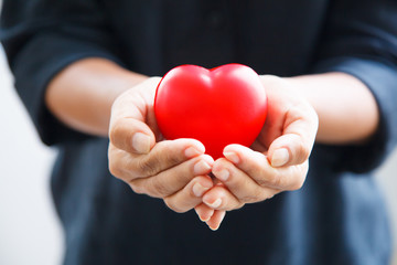 red heart in female's both hands in black suit background, represents helping hands in hard time,...