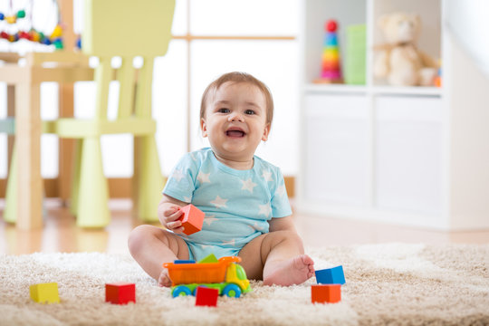 Baby boy laughing and playing with colorful toys sitting on soft carpet in nursery