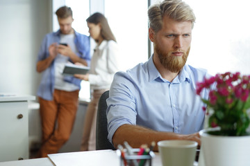 Portrait of young man sitting at his desk in the office, working on his laptop.